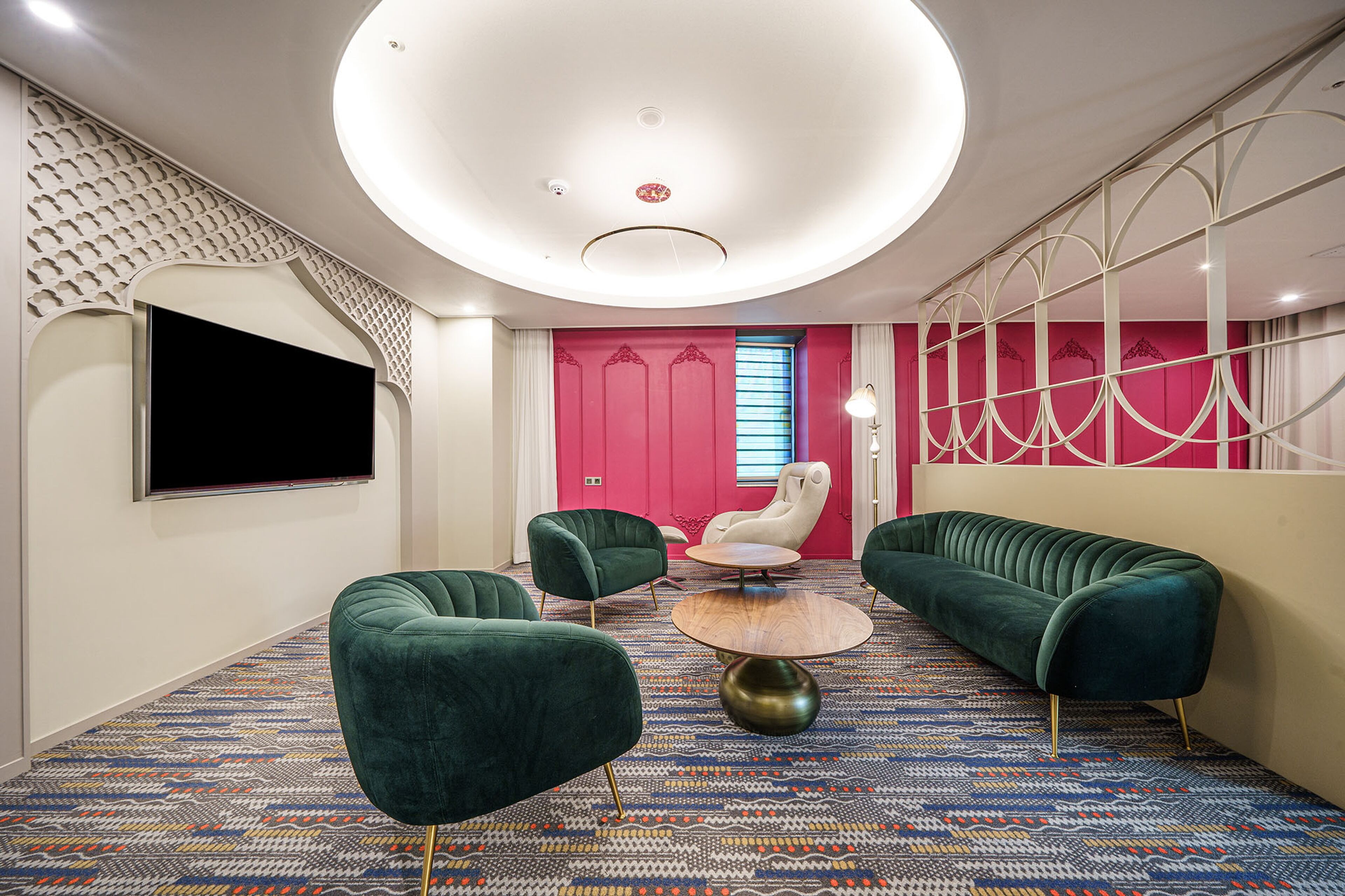 Un salon moderne avec des canapés verts, une table basse ronde et un téléviseur à écran plat fixé au mur.