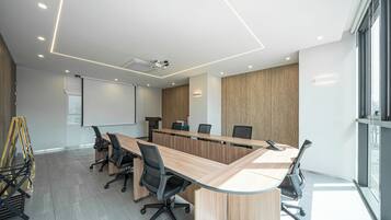 A modern conference room with a long table, black office chairs, a projector screen, and a large window.