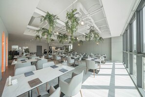 A modern dining area with tables and chairs, ceiling plants, and large windows.