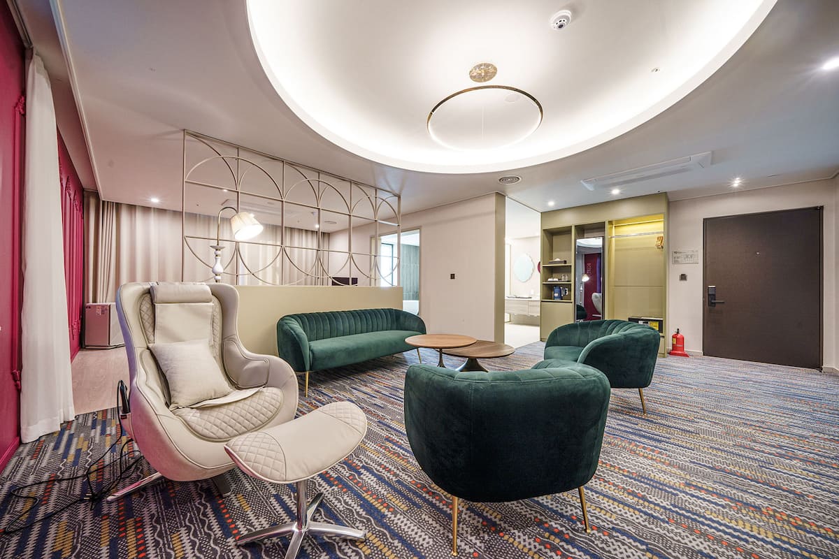 A modern hotel lobby with a green sofa, a white armchair, and a patterned carpet.