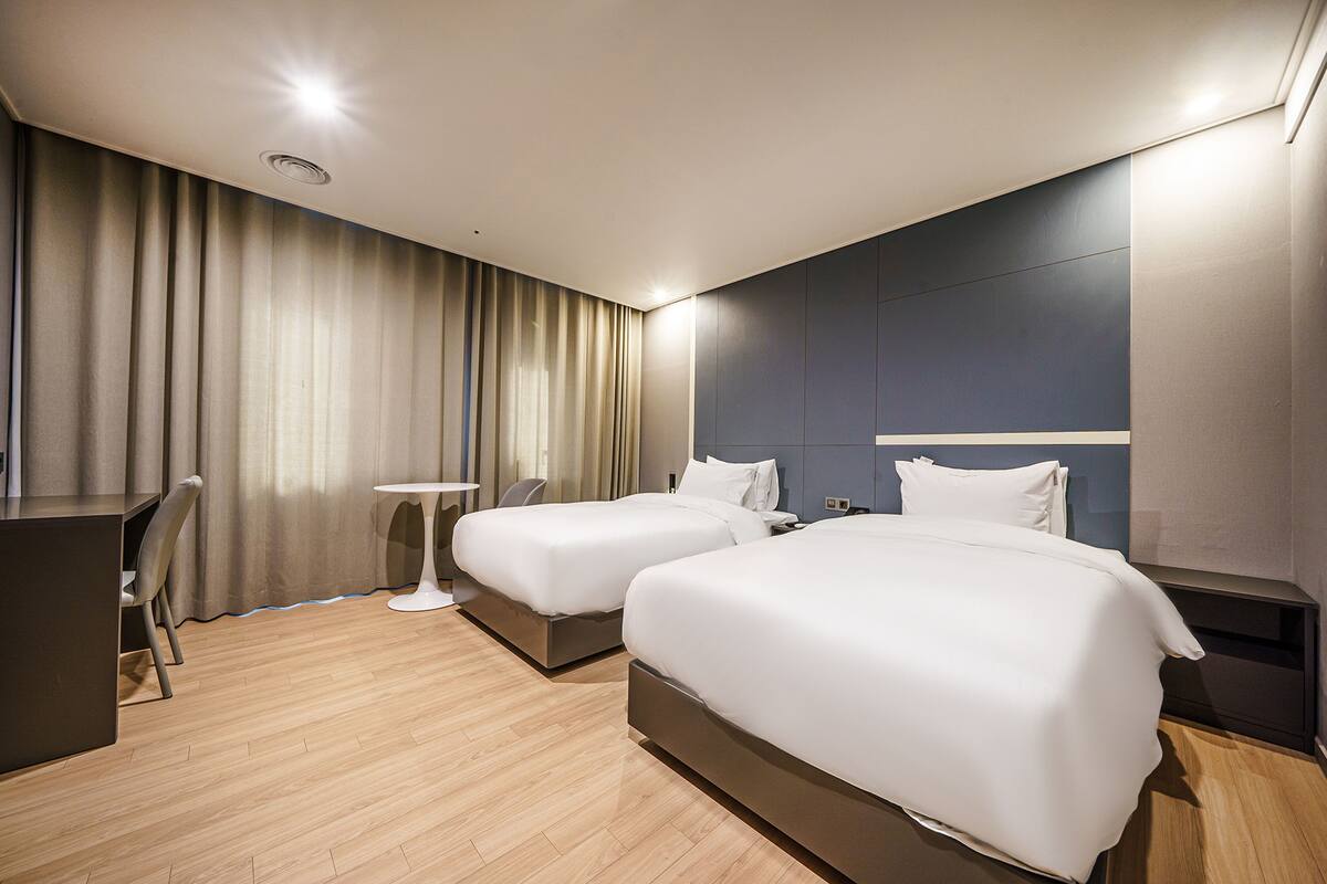 A hotel room with two beds, a desk, and a small table.