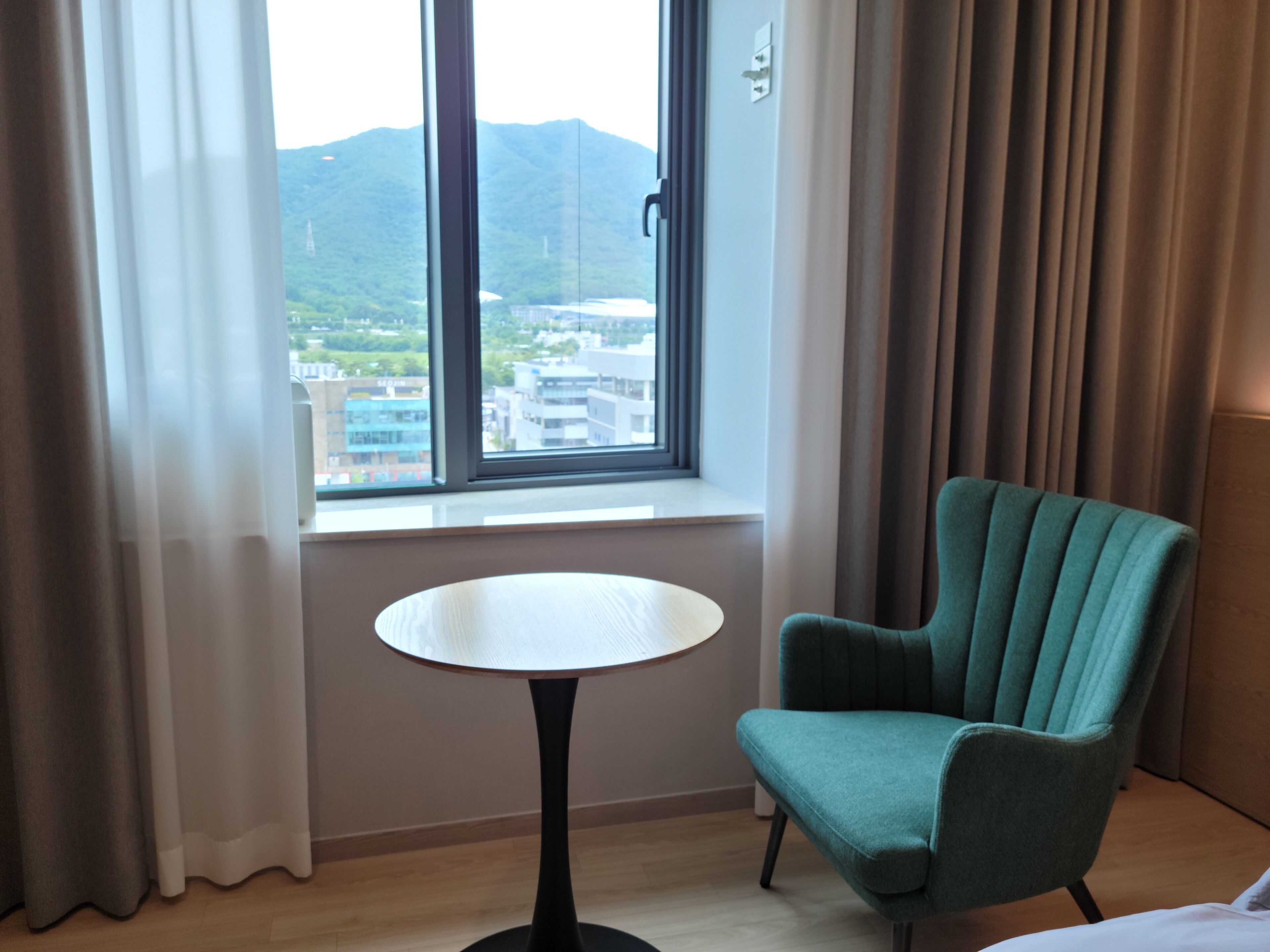 Camera d'albergo con vista sulla città e sulle montagne attraverso un'ampia finestra.