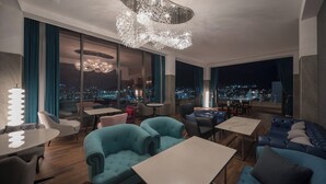 A modern lounge with a city view, featuring a unique chandelier, comfortable seating, and a mix of tables and chairs. - ACT Hotel (Daegu)
