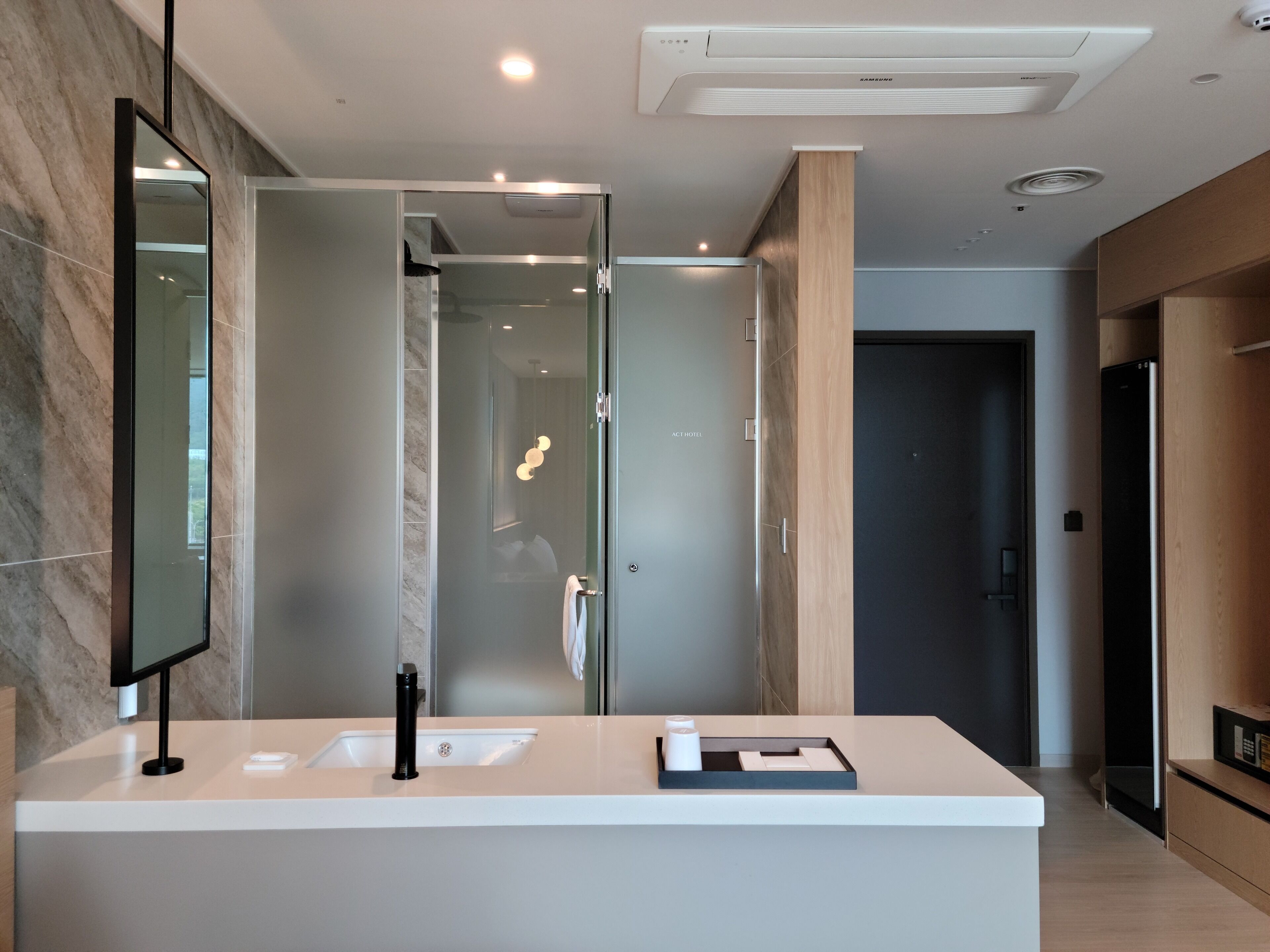 Un baño moderno con ducha acristalada, un espejo grande y un lavamanos blanco con grifo negro.