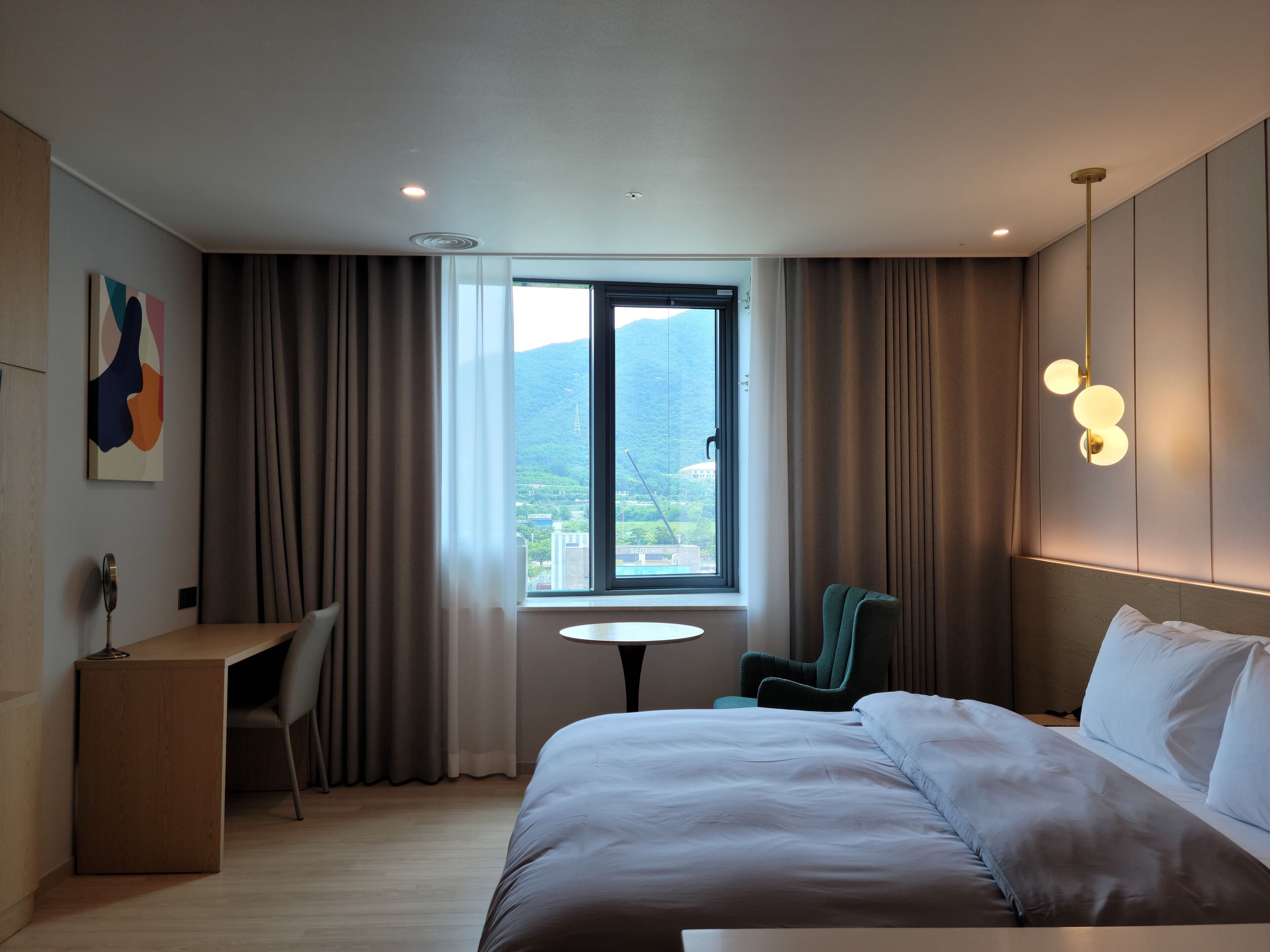 A modern hotel room with a large bed, a desk, a chair, and a small table.
