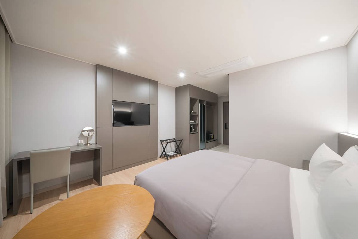 A modern hotel room with a large bed, a desk, a chair, and a TV.