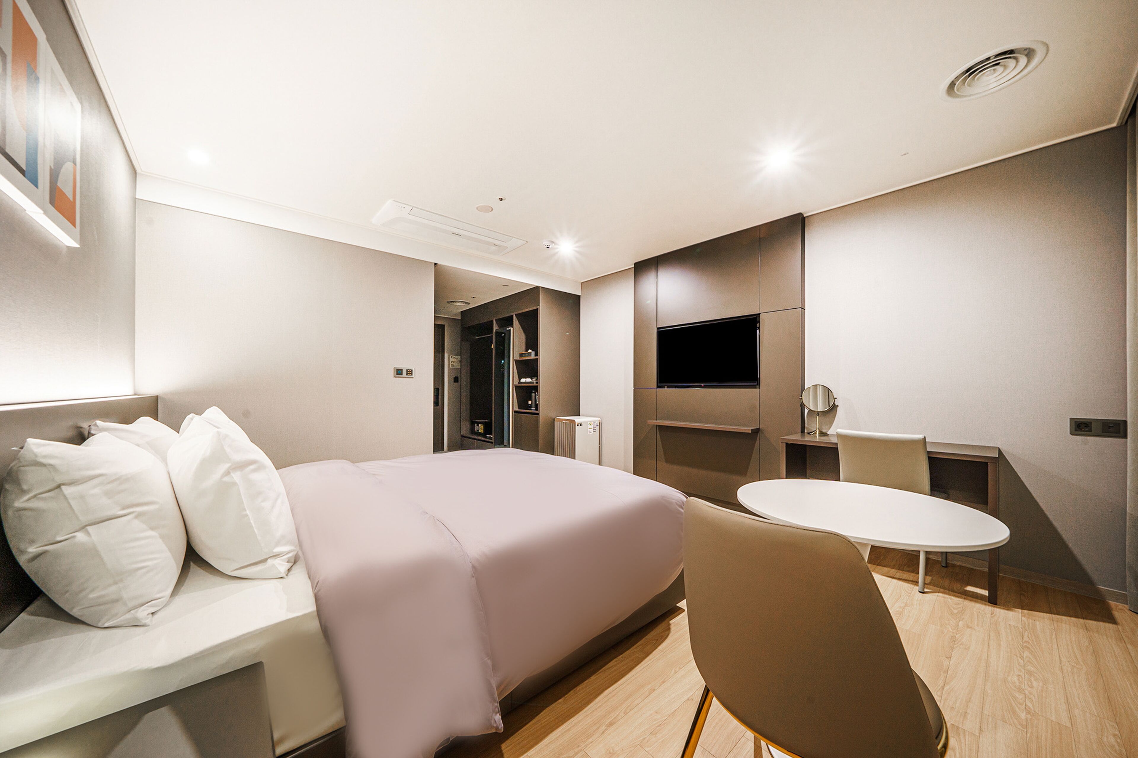 A modern hotel room with a bed, a desk, a chair, and a television.