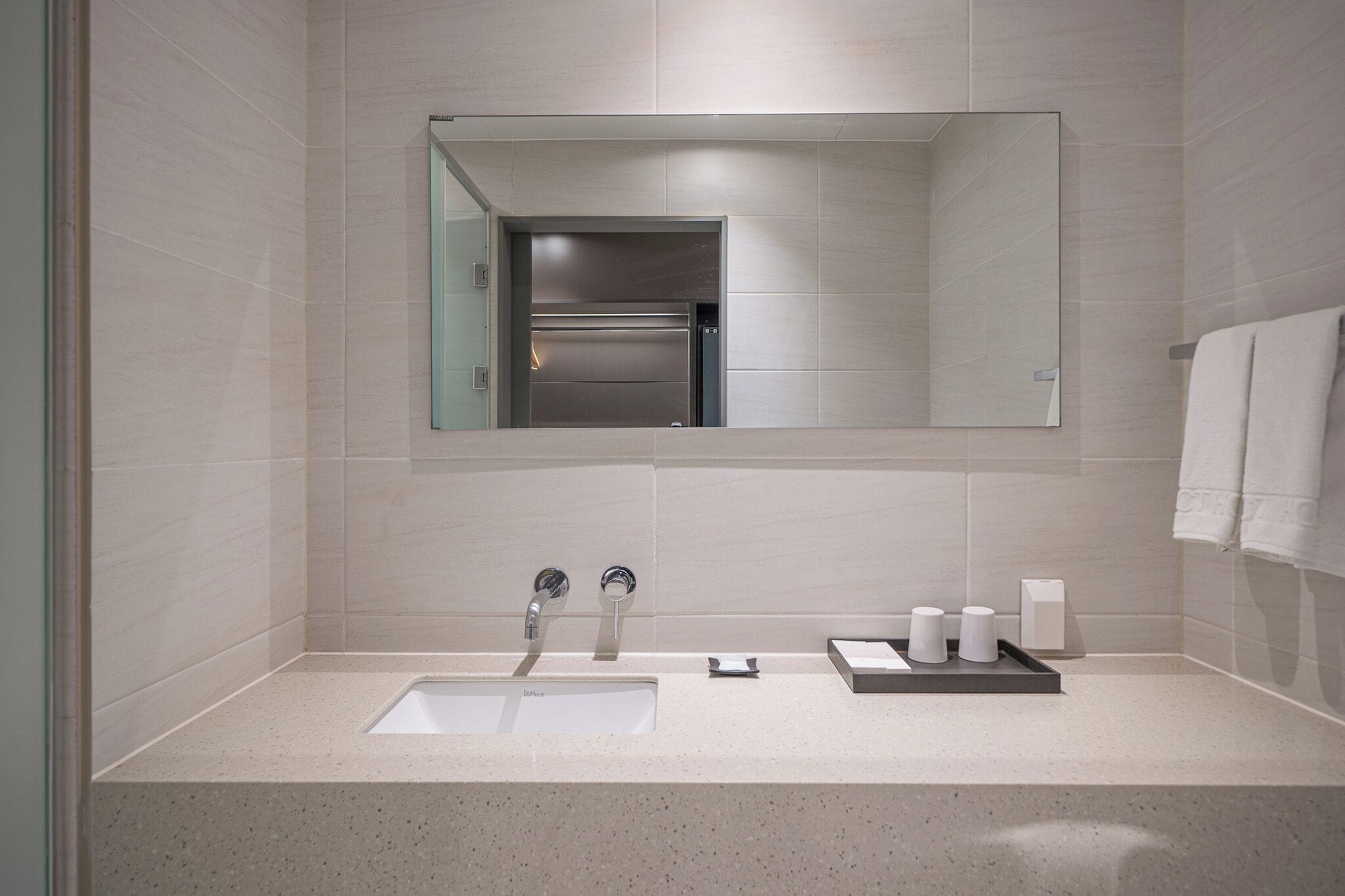 A modern bathroom with a large mirror, a sink, and a towel rack.