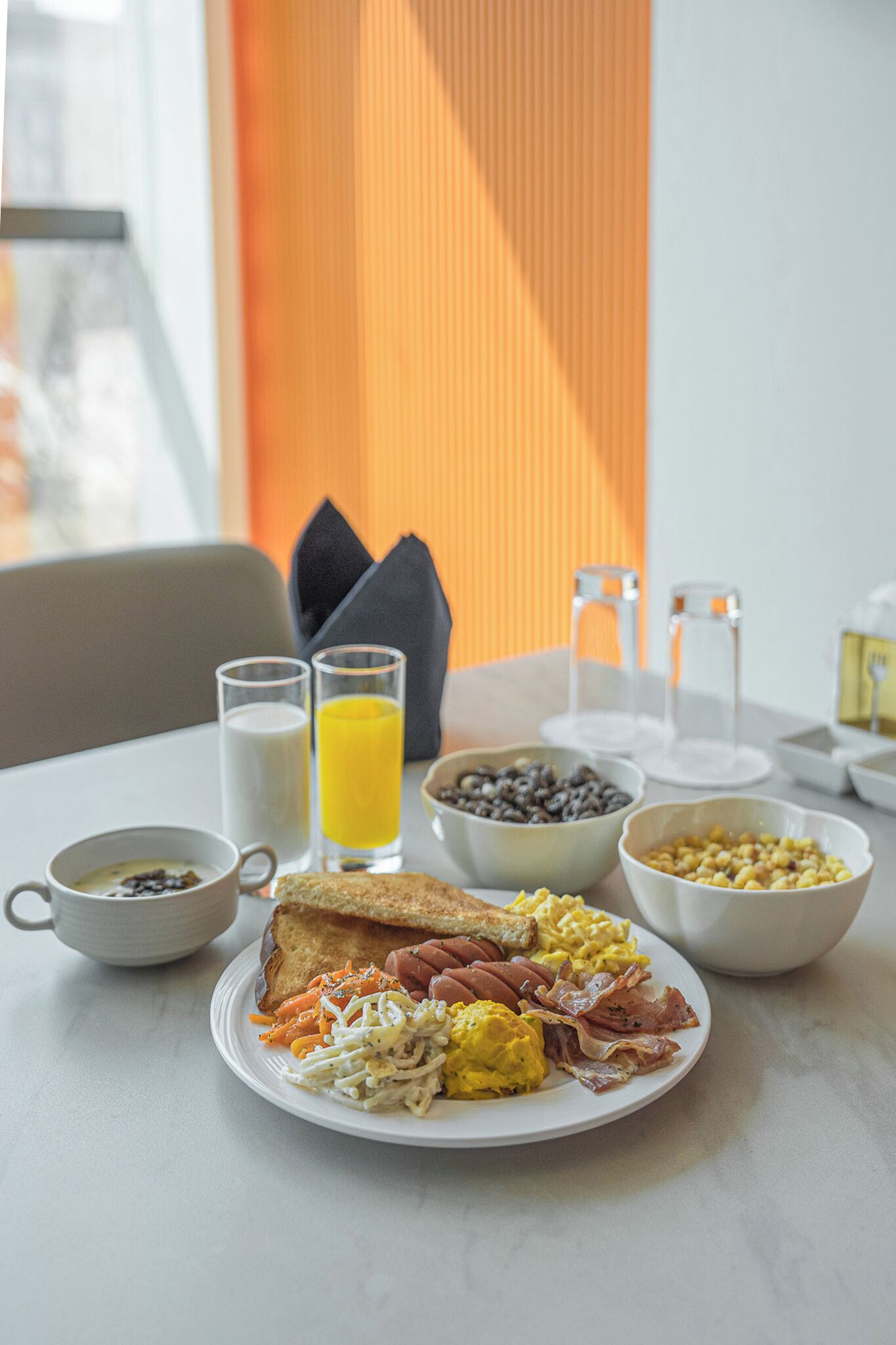 A breakfast setting with toast, eggs, bacon, and a bowl of cereal on a table.
