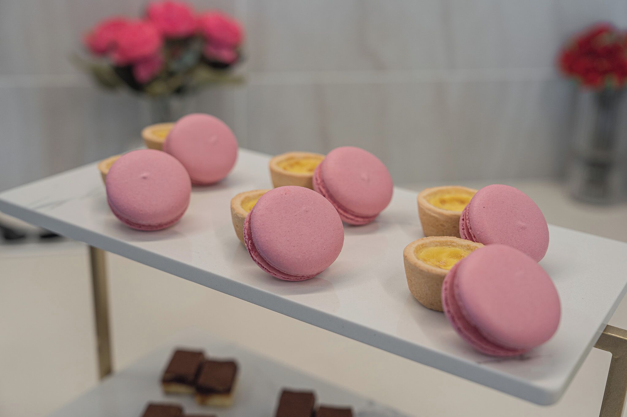 A white table with pink and yellow macarons and chocolate pieces.