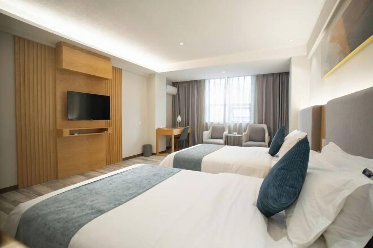 A hotel room with two beds, a TV, a desk, and a chair.