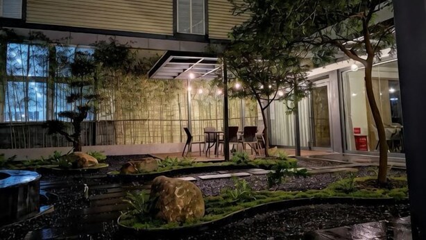 Un edificio moderno con un patio jardín, mobiliario exterior y una fuente de agua.