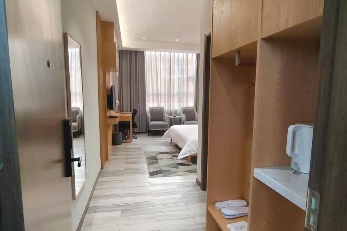 A hotel room with a bed, a desk with a chair, a TV, and a small table with a cup.