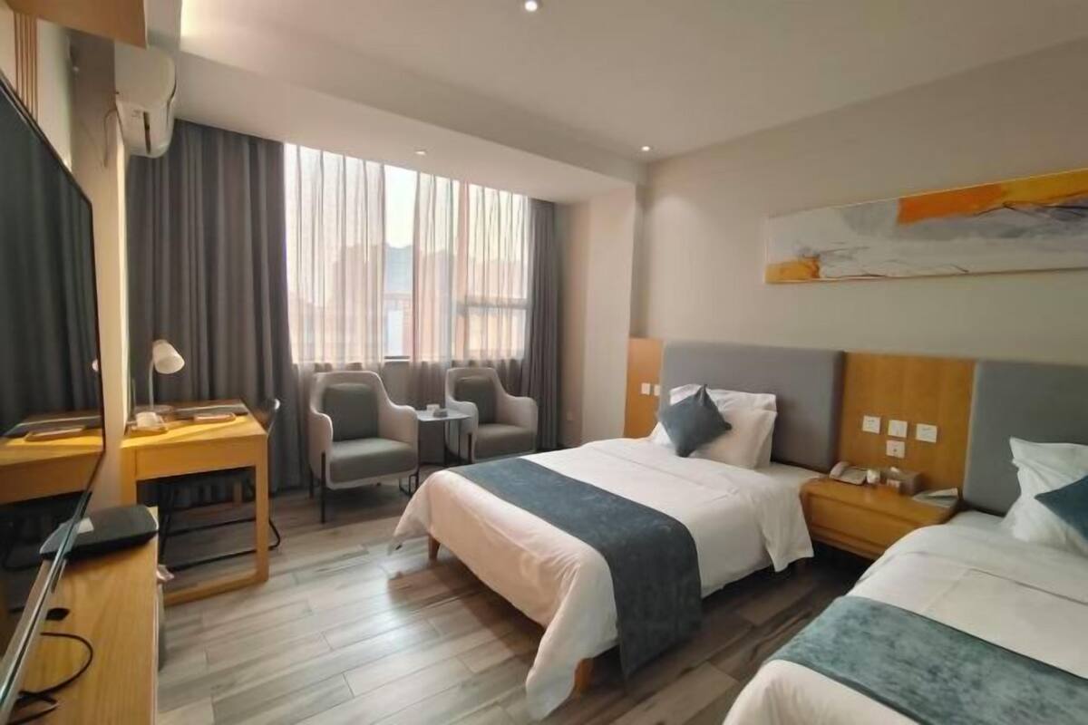 A hotel room with a bed, a desk with a chair, a small table, and a TV.