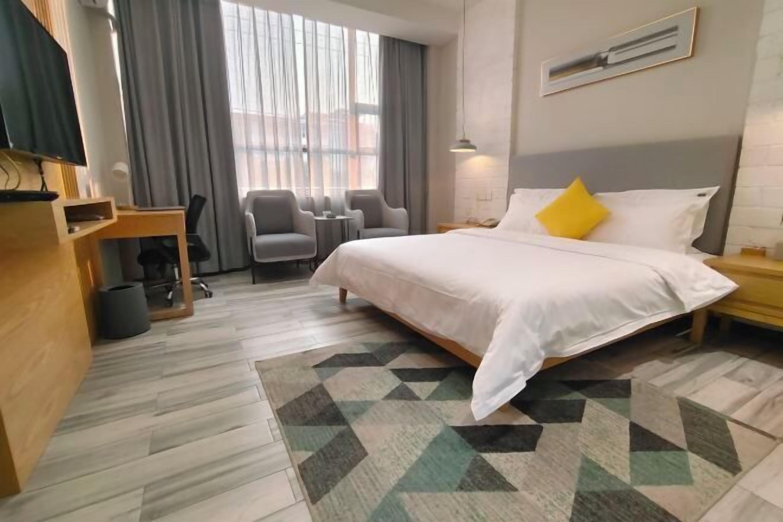 A hotel room with a bed, a desk, a chair, a TV, and a large window with curtains.