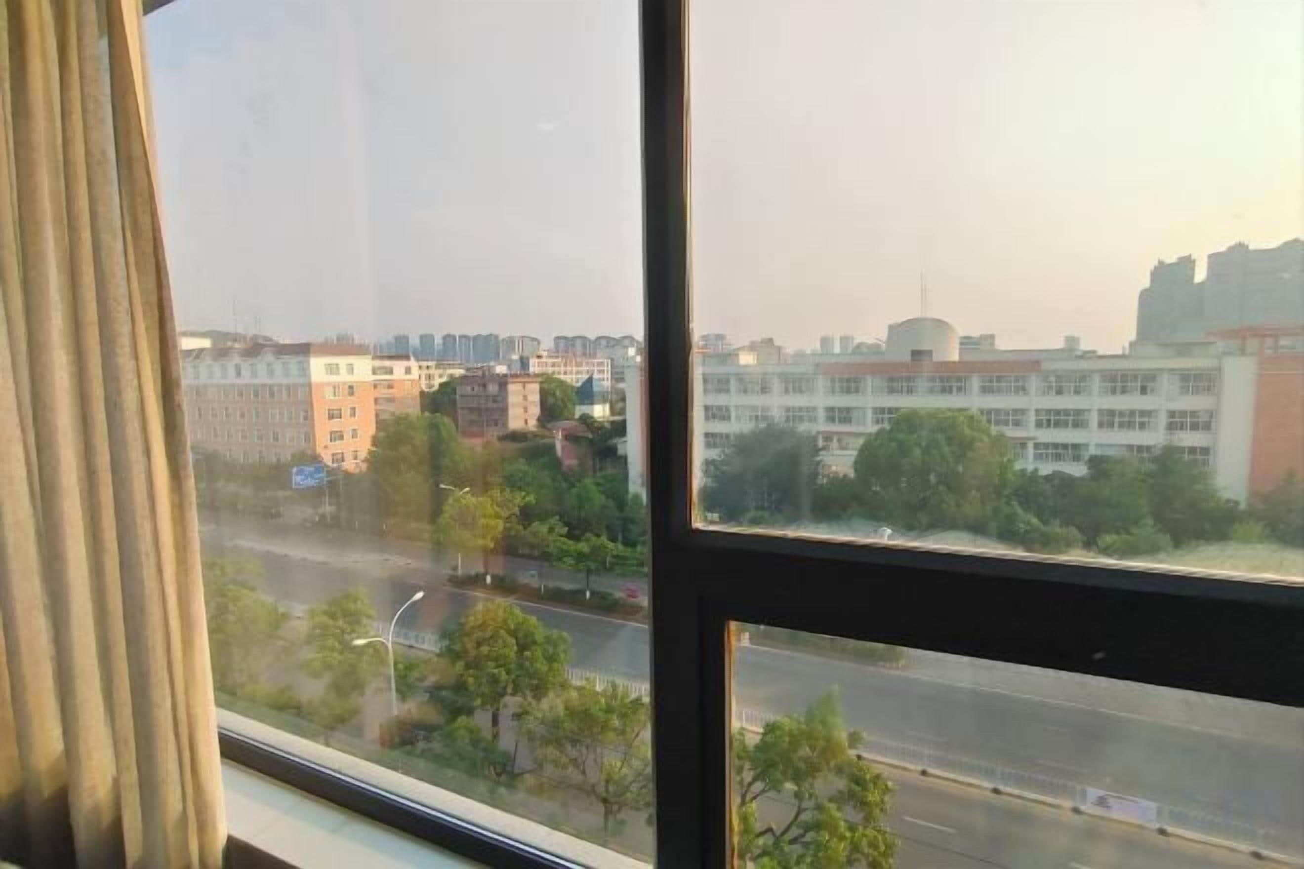 A view through a window with a curtain, overlooking a road and buildings.