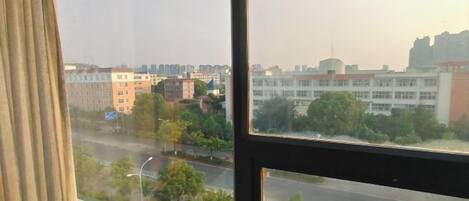 A view through a window with a curtain, overlooking a road and buildings.