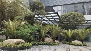 Un jardín moderno al aire libre con estructura de vidrio, diversas plantas y un sendero de piedra.