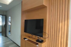 A modern living room with a flat-screen TV mounted on a wooden wall unit, a hallway with a mirror, and a door leading to another room. - Yuxi Jiada Hotel (Yuxi)