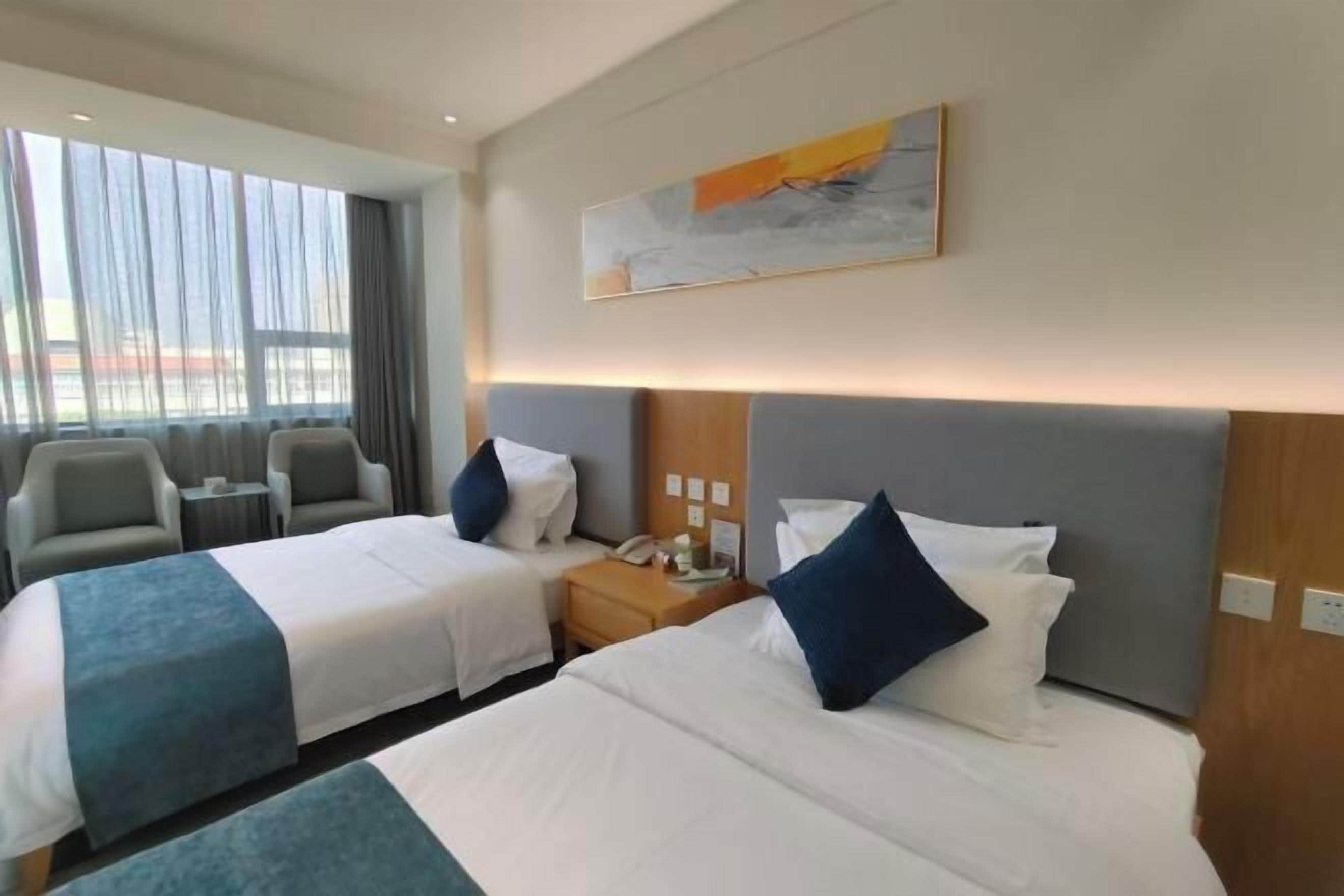 Habitació d'hotel amb dos llits, un escriptori, una cadira i una finestra gran amb cortines.