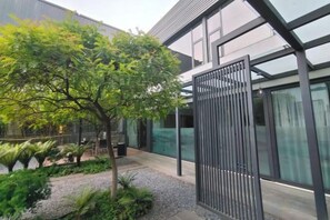 Un edificio moderno con fachada de vidrio, una reja metálica y un jardín ajardinado.