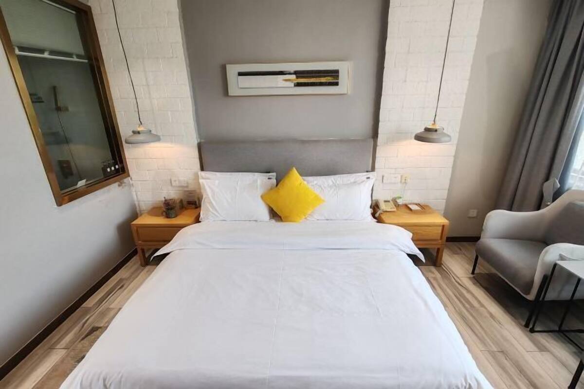 A hotel room with a large bed, two bedside tables, a chair, a modern light fixture, and a window.