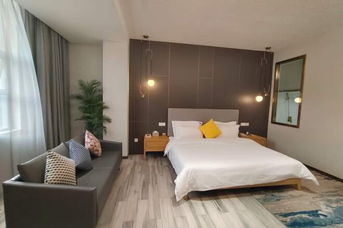 A modern hotel room with a bed, a sofa, a nightstand, a lamp, and a mirror.