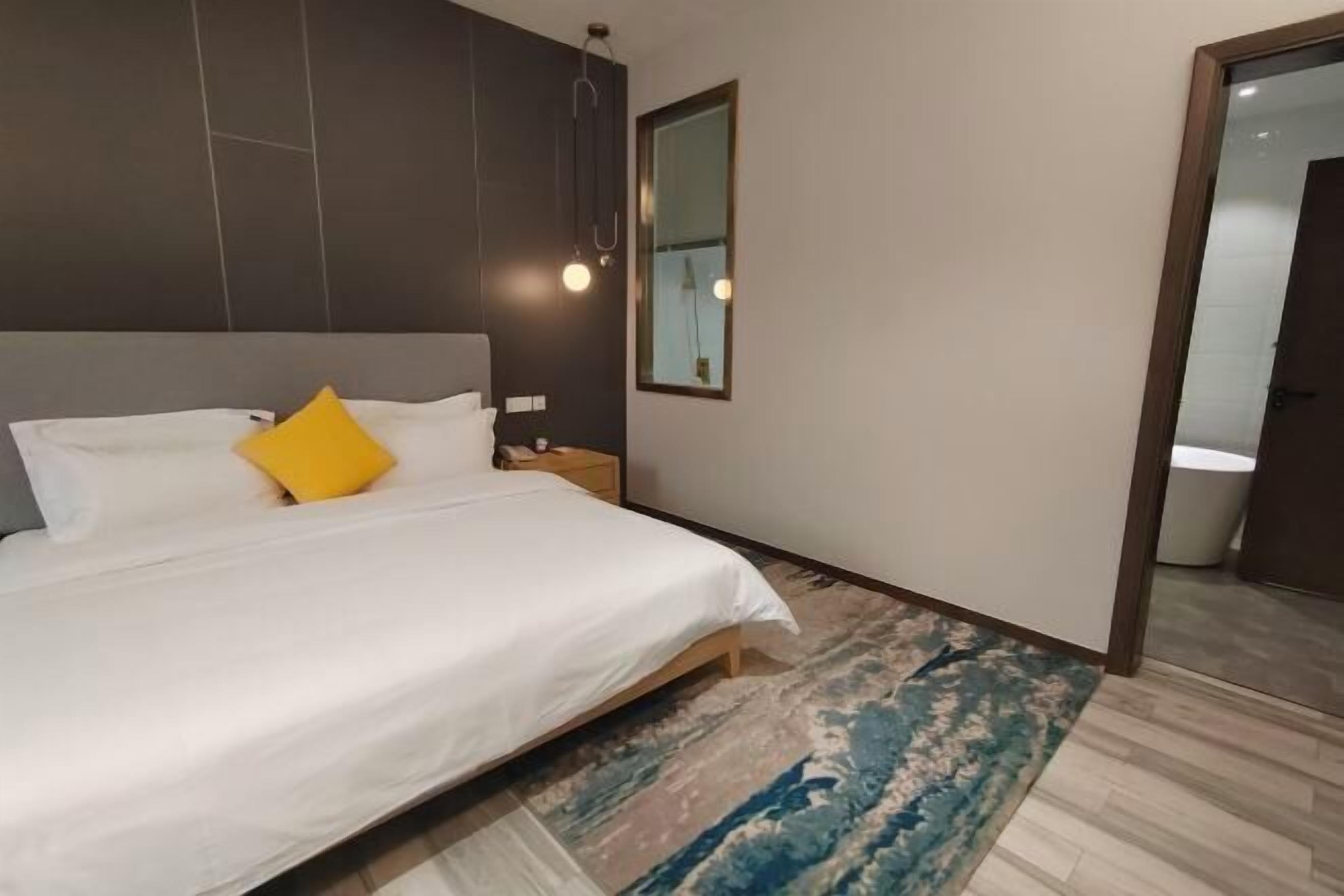 Une chambre moderne avec un grand lit, une table de chevet, un miroir et une salle de bain visible à travers une porte ouverte.