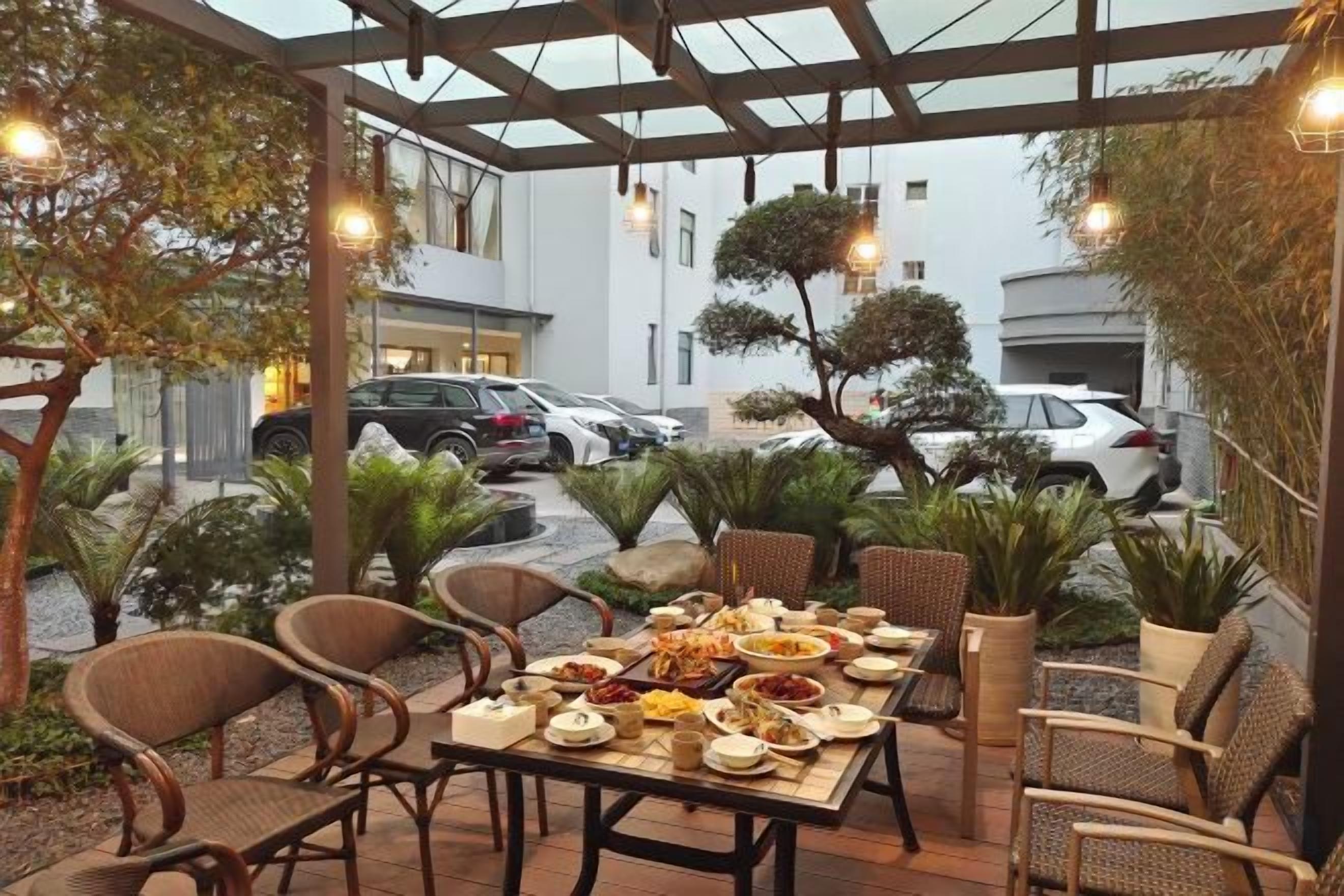 Un espace de restauration en plein air avec une table dressée pour deux personnes, entourée de chaises en osier, sous une pergola agrémentée de guirlandes lumineuses.