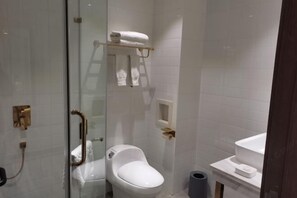 A bathroom with a glass shower enclosure, a white toilet, a sink, and a towel rack.