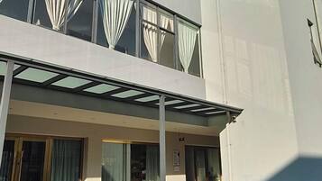 A modern building with a flat facade, large windows with curtains, and a covered outdoor area.