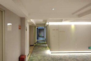 A hotel corridor with a carpeted floor, a reception area with a counter, and a door leading to a room.