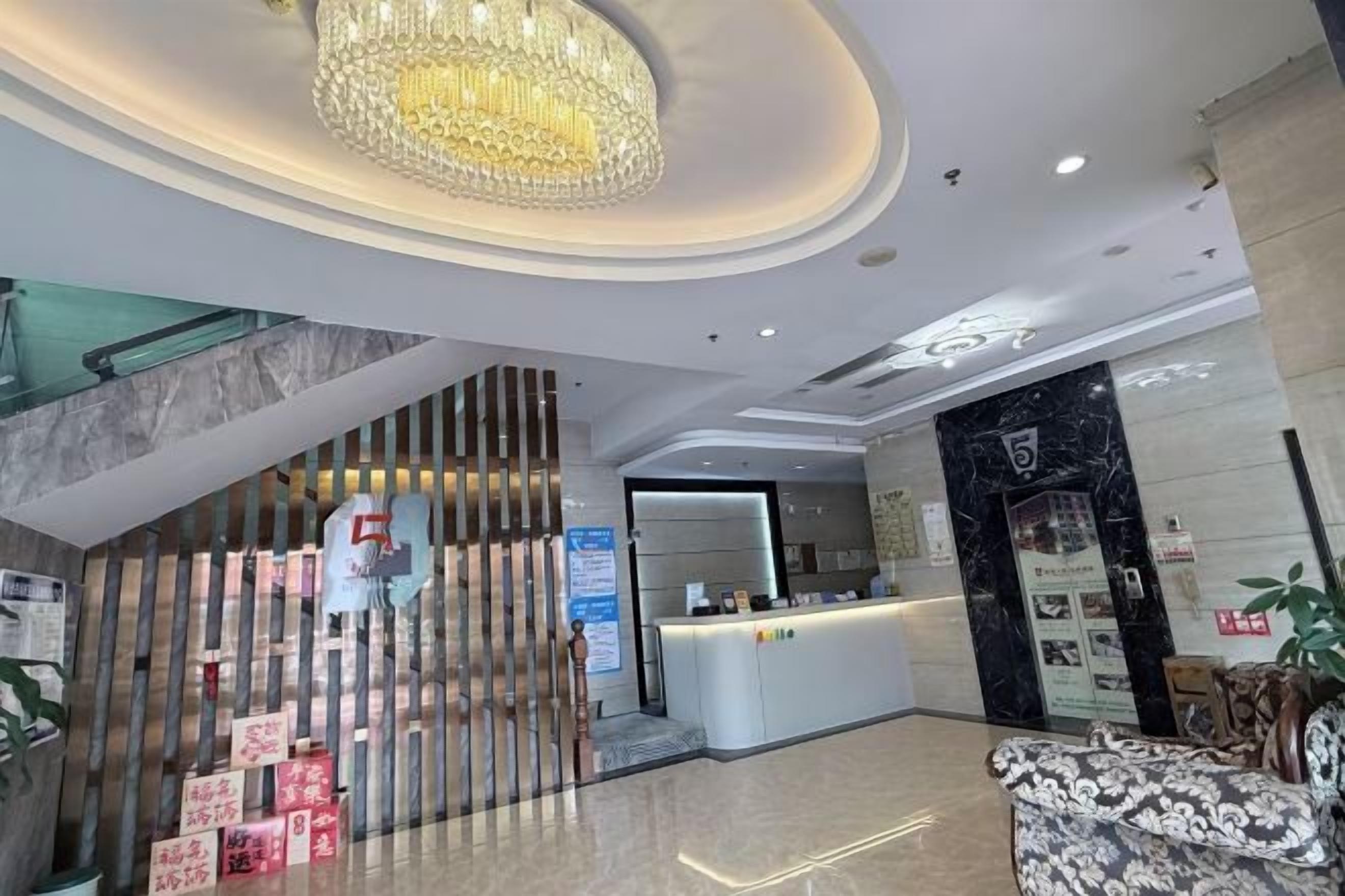 A hotel lobby with a reception desk, a chandelier, and a staircase leading to an upper level.