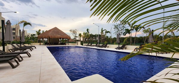 Relax by the resort pool surrounded by lounge chairs and umbrellas, with a bar nearby.