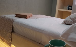 Cozy retreat with a neatly made bed, featuring a comfortable pillow and a convenient shelf for personal items.