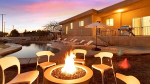 Un área de piscina con sillones reclinables, un hogar y un edificio con terraza cubierta.