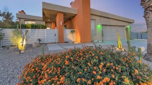 Un edificio moderno con techo plano, ventanas amplias y un patio con cactus y flores de clavelina.