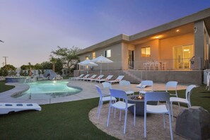 A modern outdoor pool area with lounge chairs, a fire pit, and a covered seating area.