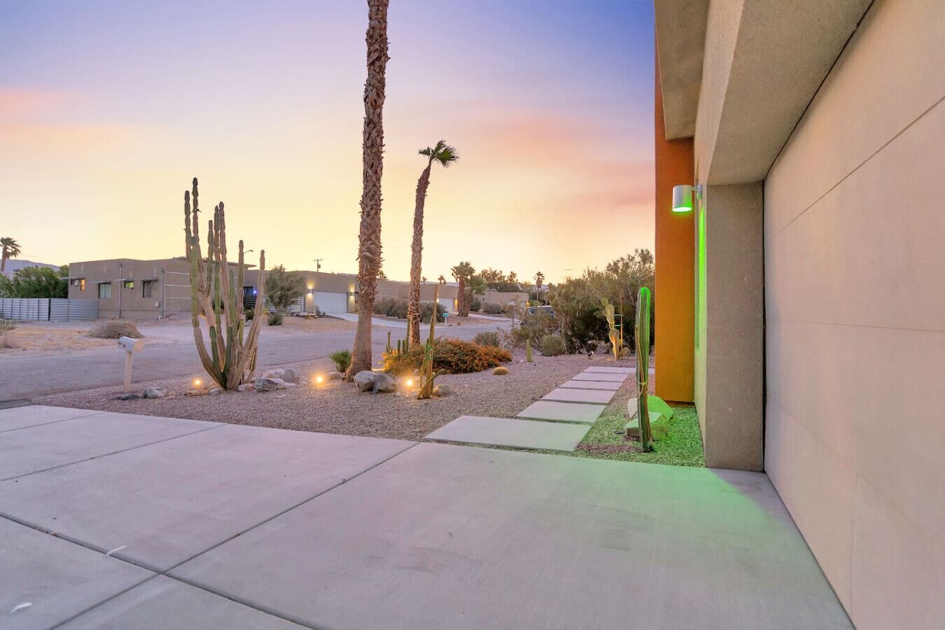Un paysage désertique avec des palmiers, des cactus et un chemin pavé menant à un bâtiment.