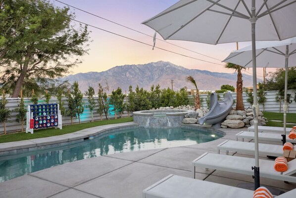 A swimming pool with a mountain backdrop, lounge chairs, and a game board.