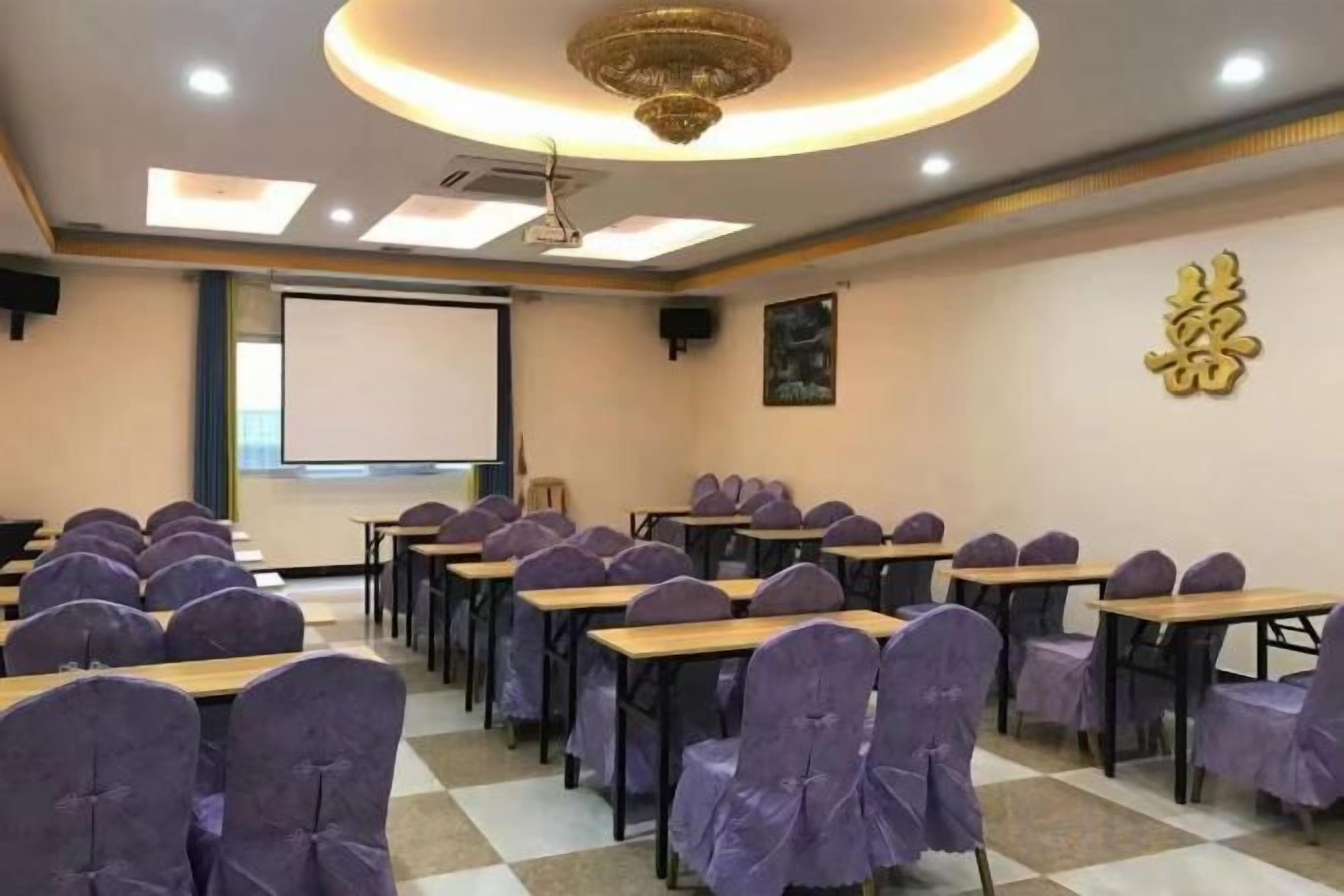 A conference room with rows of tables and chairs, a projector screen, and a ceiling light fixture.