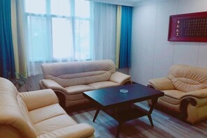 Una sala de estar con sofás color beige, una mesa de centro negra y un ventanal con cortinas azules.