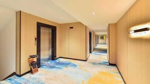 Un pasillo de hotel con piso alfombrado, un cesto de basura y una lámpara fijada a la pared.