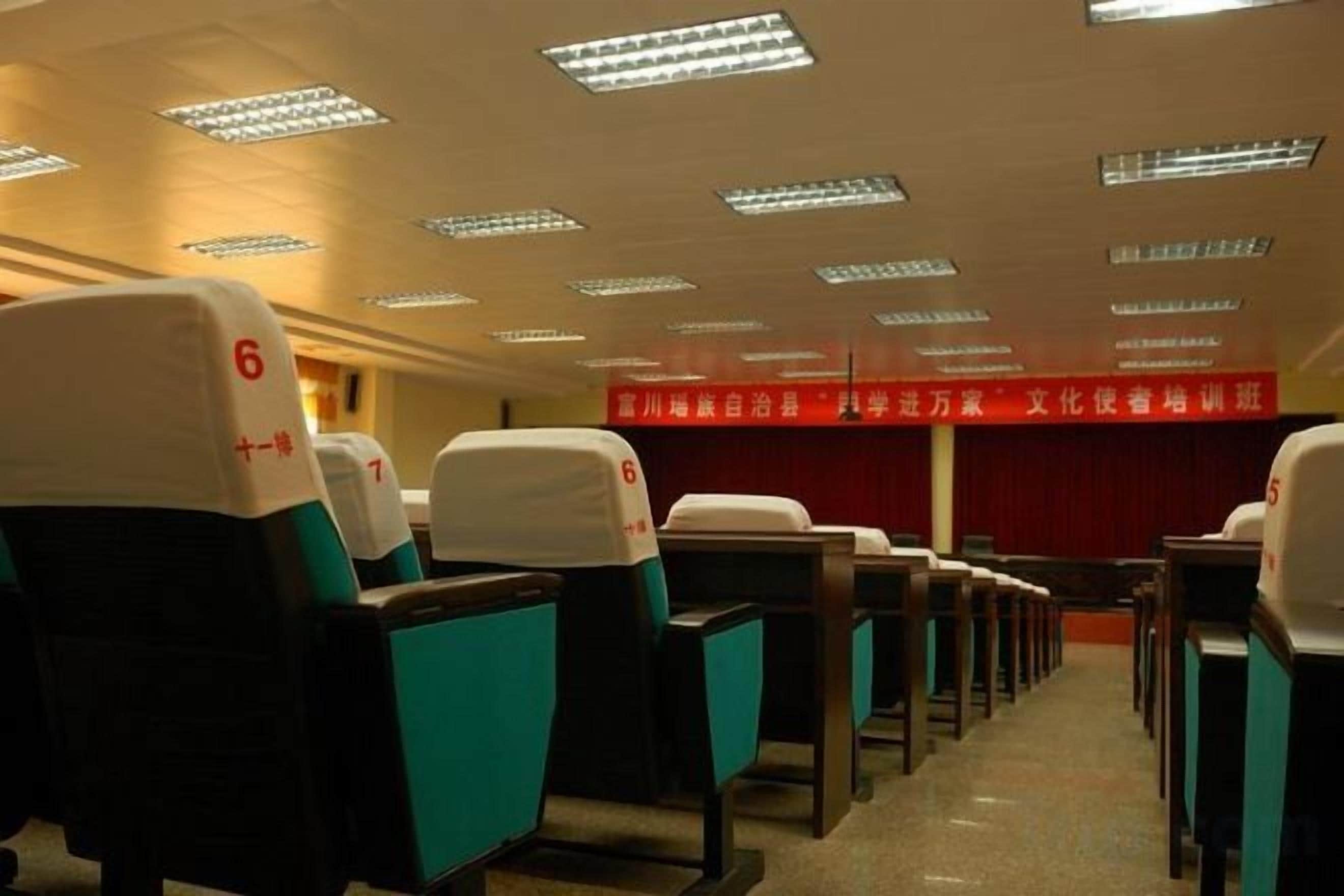 A conference room with rows of chairs, a stage with a red curtain, and a banner with text.