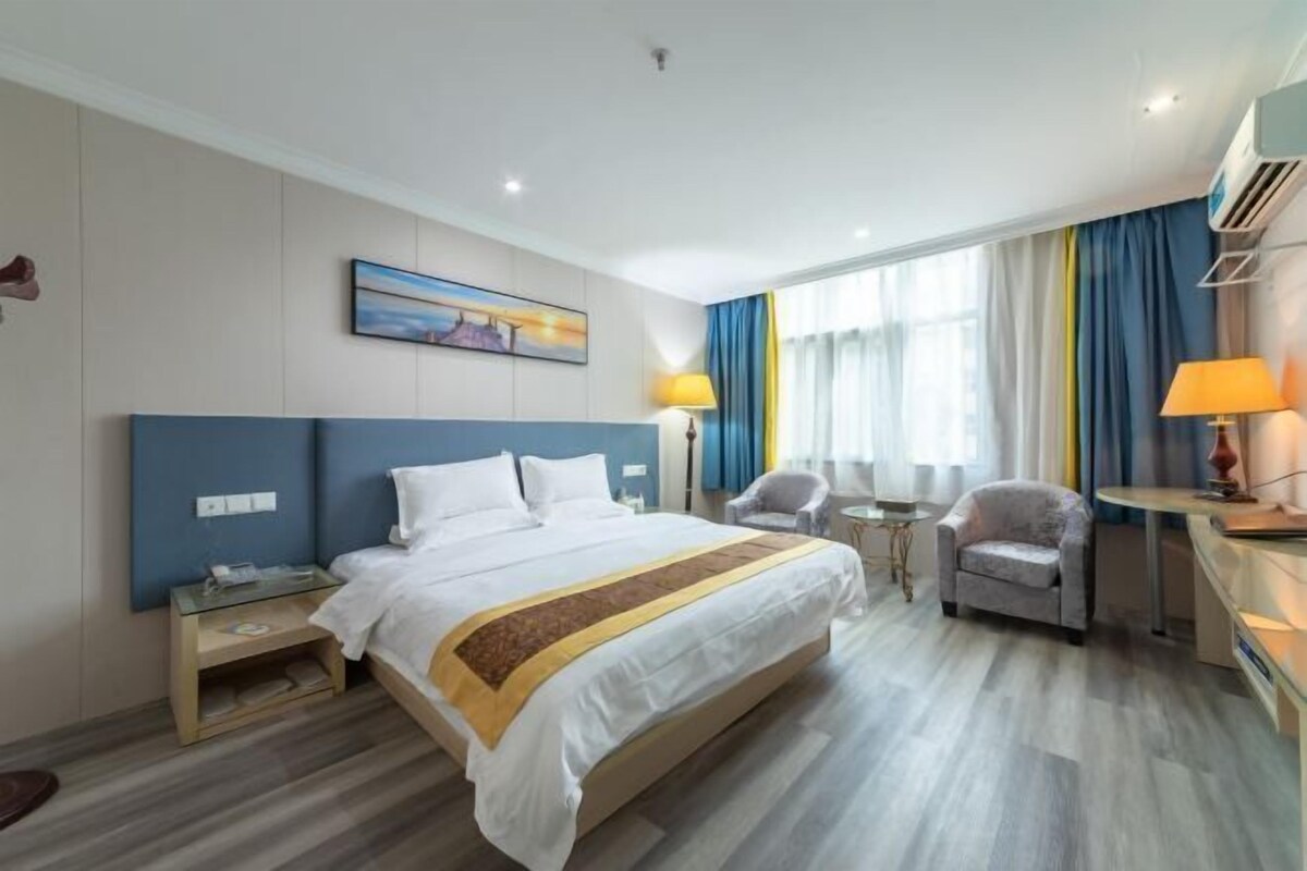 Una habitación de hotel con cama, mesitas de noche, un escritorio, una silla y una ventana con cortinas.