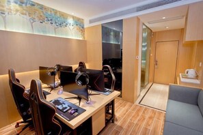 Een moderne hotelkamer met een bureau, gamingstoelen, een bank en een groot raam.