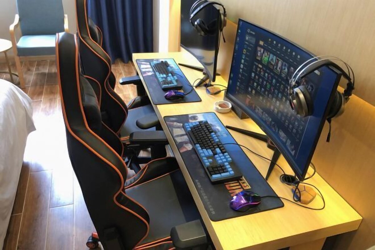 A hotel room with a gaming setup including two keyboards, a monitor, and headphones.