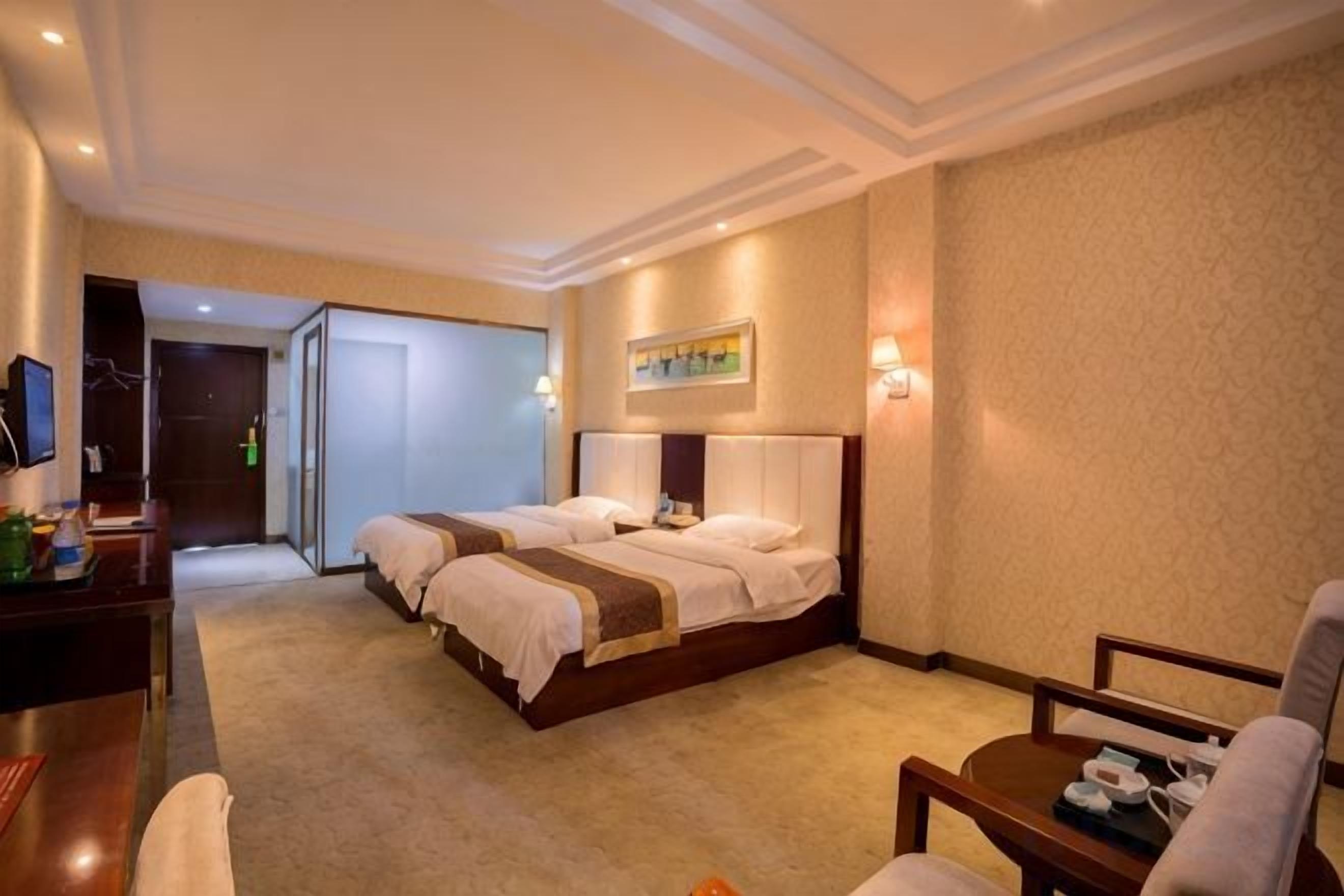 A hotel room with two beds, a desk, a chair, and a television.