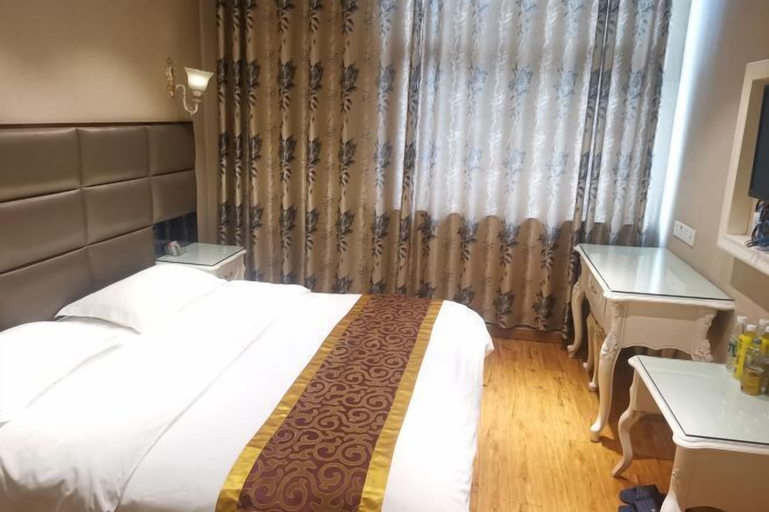 A hotel room with a bed, a nightstand, a desk, and a window with curtains.