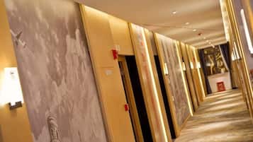 Un couloir d’hôtel avec des portes, un sol recouvert de moquette et un mur orné d’une fresque représentant un paysage urbain.